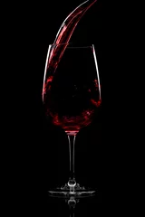 Poster Red wine pouring into a wine glass, over black background, © alesmunt