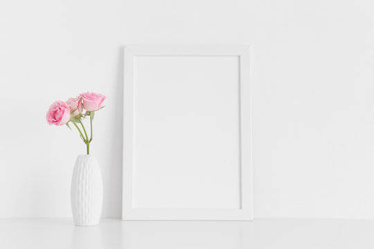 White frame mockup with pink roses in a vase on a white table.Portrait orientation.