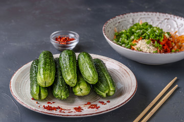 Preparing products for cooking traditional Korean cucumber kimchi snack: cross-cut cucumbers in the foreground, mixing ingredients in a bowl, fermented food, horizontal photo