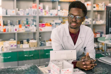 Gordijnen Ervaren Afro-Amerikaanse man apotheker in witte jas werken in moderne apotheek © sofiko14