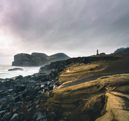 View over Capelinhos volcano, lighthouse of Ponta dos Capelinhos on western coast on Faial island, Azores, Portugal with a dramatic sunset and strong waves and clouds. Last volcano eruption was in