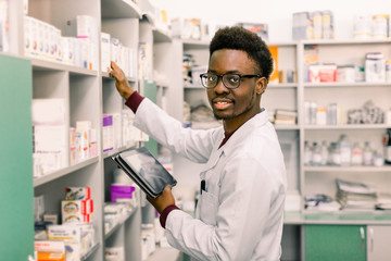 African American male pharmacist using digital tablet during inventory in pharmacy.
