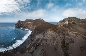 Fototapeta na wymiar View over Capelinhos volcano, lighthouse of Ponta dos Capelinhos on western coast on Faial island, Azores, Portugal on a sunny day with blue sky and clouds and waves. Last volcano eruption was in 1957