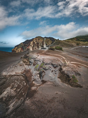 View over Capelinhos volcano, lighthouse of Ponta dos Capelinhos on western coast on Faial island, Azores, Portugal on a sunny day with blue sky and clouds and waves. Last volcano eruption was in 1957