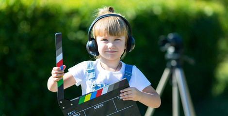 Portrait of a child with a TV clapper. Television numerator. A little girl in headphones with a TV...