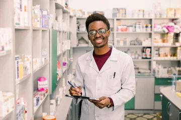 Wall murals Pharmacy Smiling African American man pharmacist or Chemist Writing On Clipboard While standing in interior of pharmacy