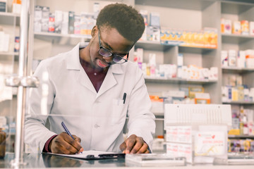 Portret van een gelukkige Afro-Amerikaanse apotheker die een recept schrijft op de werkplek in een moderne apotheek