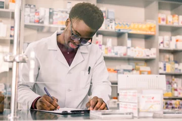 Poster de jardin Pharmacie Portrait d& 39 un pharmacien afro-américain heureux écrivant une ordonnance sur le lieu de travail dans une pharmacie moderne
