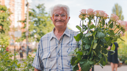 Portrait of an elderly man standing on the street with a bouquet of roses.