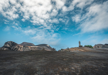 View over Capelinhos volcano, lighthouse of Ponta dos Capelinhos on western coast on Faial island, Azores, Portugal on a sunny day with blue sky and clouds and waves. Last volcano eruption was in 1957
