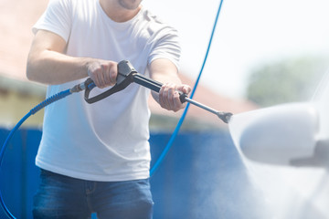 Fashionable man washing car with pressurized water in car wash.