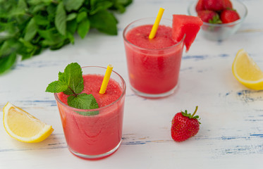 Cold watermelon smoothie with mint, lemon and strawberries in glasses . Colorful refreshing drinks for summer, on wooden light blue background.