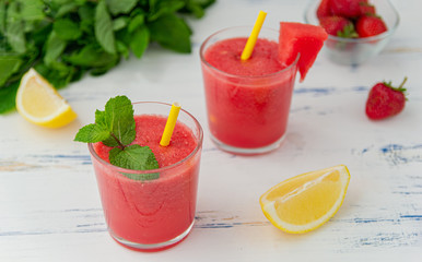 Cold watermelon smoothie with mint, lemon and strawberries in glasses . Colorful refreshing drinks for summer, on wooden light blue background.