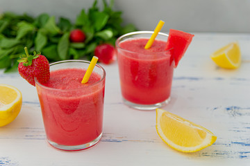 Cold watermelon smoothie with mint, lemon and strawberries in glasses . Colorful refreshing drinks for summer, on wooden light blue background.