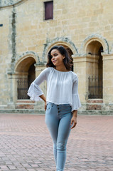 Fototapeta na wymiar Outdoor portrait of young beautiful girl 9 to 25 years old posing in street. wearing white blouse and tight jeans and sapatillas. City lifestyle. Female fashion concept.