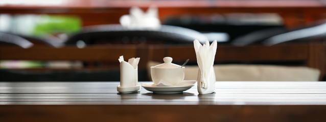 Table in a cafe or restaurant. White napkins, spices and sugar on a wooden table, panoramic view