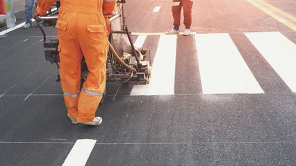 Road workers with thermoplastic spray road marking machine working to paint pedestrian crosswalk on asphalt road surface in the city - obrazy, fototapety, plakaty