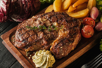 Ribeye steak with potatoes, onions and baked cherry tomatoes. Juicy steak with flavored butter