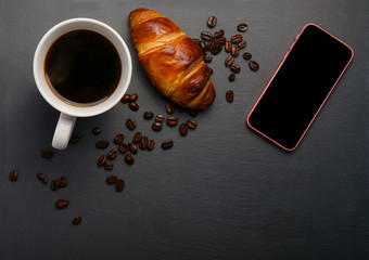 Fresh croissants and coffee and roasted beans on stone table. Top view with copy space. Coffee mug on black background. white coffee mug and croissant on black background. 