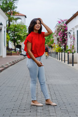 Outdoor portrait of young beautiful girl 19 to 25 years old. Brunette. posing in the middle of a colonial street with cobblestones. Wearing red blouse City lifestyle. Female fashion concept.