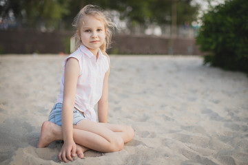 eautiful little girl sitting on the sand in the desert at sunset.
