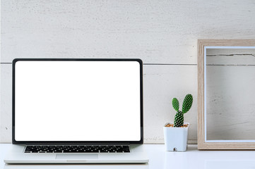 Mockup white blank screen laptop, wooden picture frame and green cactus flower on white table.