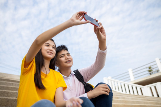 boy and girl friend sitting selfie with smartphone on holding hand in the park