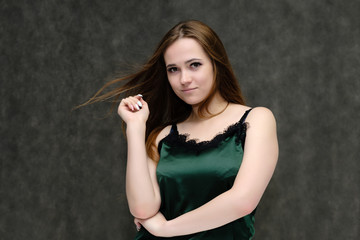 Concept portrait of the waist of a pretty girl, a young woman with long beautiful brown hair and a green T-shirt on a gray background. In the studio in different poses showing emotions.