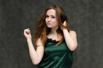 Concept portrait of the waist of a pretty girl, a young woman with long beautiful brown hair and a green T-shirt on a gray background. In the studio in different poses showing emotions.