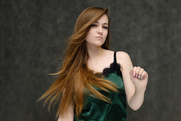 Concept portrait of the waist of a pretty girl, a young woman with long beautiful brown hair and a green T-shirt on a gray background. In the studio in different poses showing emotions.