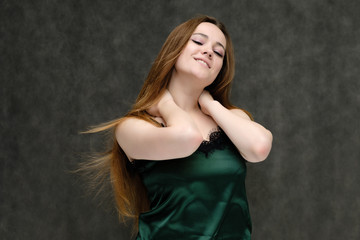 Obraz premium Concept portrait of the waist of a pretty girl, a young woman with long beautiful brown hair and a green T-shirt on a gray background. In the studio in different poses showing emotions.
