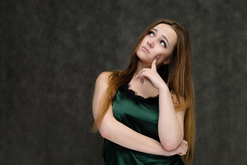 Fototapeta premium Concept portrait of the waist of a pretty girl, a young woman with long beautiful brown hair and a green T-shirt on a gray background. In the studio in different poses showing emotions.
