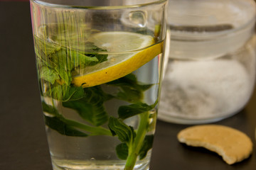 there is a glass with green tea, lemon and a sprig of mint. A sugar bowl with a spoon and a biscuit is worth a row with a glass.