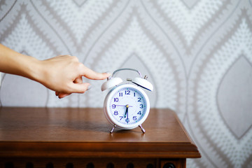 Close-up of woman in bed extending hand to alarm clock. Morning