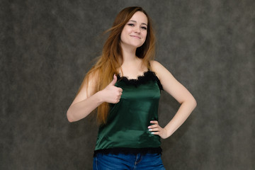 Concept portrait below belt of pretty girl, young woman with long beautiful brown hair and green t-shirt and blue jeans on gray background. In the studio in different poses showing emotions.