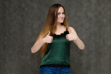 Concept portrait below belt of pretty girl, young woman with long beautiful brown hair and green t-shirt and blue jeans on gray background. In the studio in different poses showing emotions.