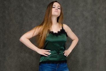 Obraz na płótnie Canvas Concept portrait below belt of pretty girl, young woman with long beautiful brown hair and green t-shirt and blue jeans on gray background. In the studio in different poses showing emotions.