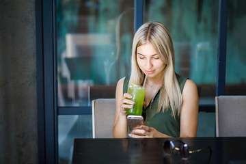 A young beautiful blonde girl sits in a cozy cafe, talks on the phone and drinks a cooling drink. Rest in the summer heat