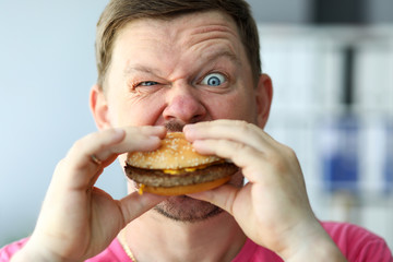 Funny bearded man with idiot facial expression eating big burger