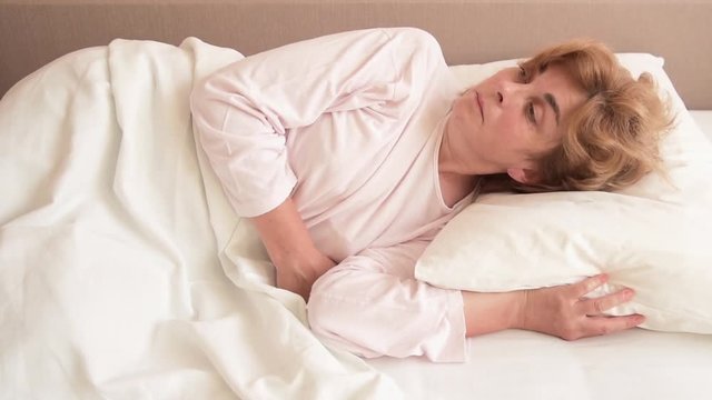 Exhausted mature woman in bed waking up and falling back to sleep   