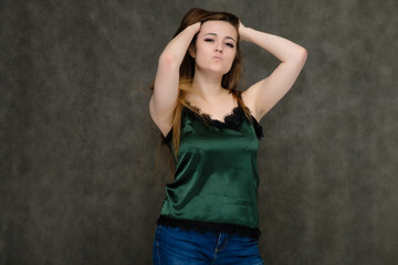 Naklejka premium Concept portrait below belt of pretty girl, young woman with long beautiful brown hair and green t-shirt and blue jeans on gray background. In the studio in different poses showing emotions.