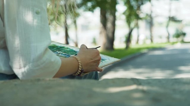 Close Up of Female Street Artist Drawing an Embankment with Watercolor. Woman Painting on a Canvas in Sunny Summer Day. Slow Motion. Art, Creativity and People concept