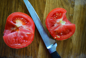 Juicy halves of red tomatoes cut with knife in halves on wooden board.