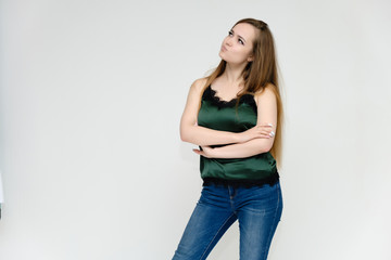 Concept portrait above the knee of a pretty girl, a young woman with long beautiful brown hair and a green t-shirt and blue jeans on a white background. In studio in different poses showing emotions.