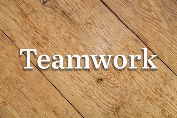 `Teamwork` white text on a wooden home background. 