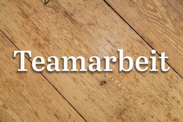 `Teamarbeit` white text on a wooden home background. Translation: `Teamwork`