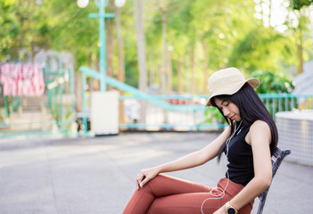 Portrait of asian women sit on the bench relaxing with green nature backgound, Girl listen musics in the morning, Rest on vacation with nature forest, Smilling and chilling girl, Lifestyle concept