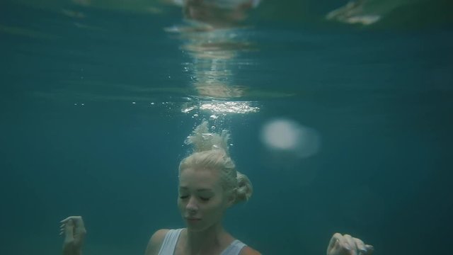 Beautiful  blonde woman emerges from the water in the sea on travel vacation. Slow motion. Young tourist female swimming in Mediterranean sea, diving into water.