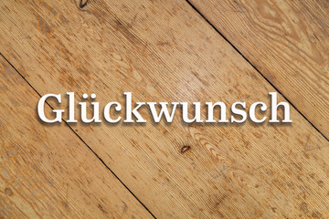 `Glückwunsch` white text on a wooden background. Translation: `Congratulations`