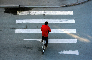 A man in a red jacket on a bicycle crosses the road at a pedestrian crossing. View from window